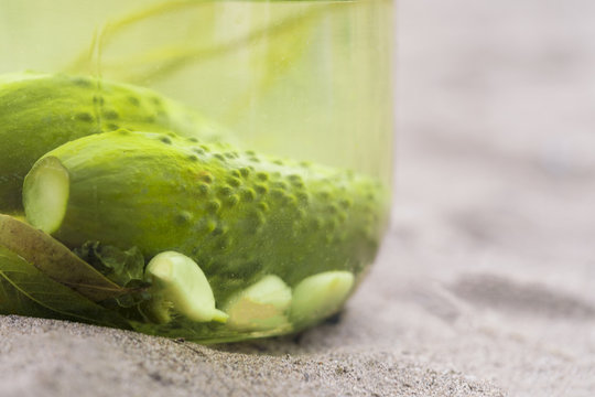 Pickled cucumbers with garlic in a glass jar on sand