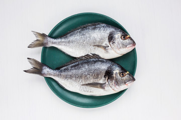 Raw dorado fish on yellow plate with peppercorns on white table. Top view, copy space 