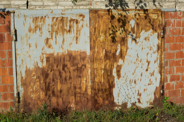 Garage building with rusty doors. Greens and shadow around him.
