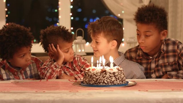 Boys near cake with candles. Kids sitting at the table. Company of friends celebrates birthday. Wish you all the good.