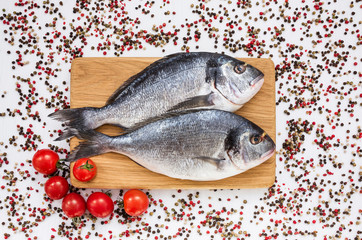 Raw dorado fish on yellow plate with peppercorns on white table. Top view, copy space 