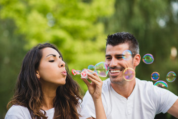 Young couple blowing bubbles. Man and woman dating and having fun at the park.