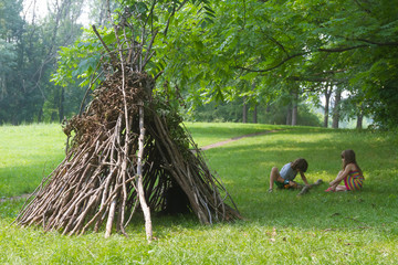 kids playing next to wooden stick house looking like indian hut,