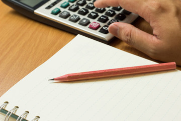 Business man place hand on calculator with pencil, book on wood