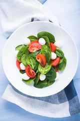 Fresh salad with mozzarella cheese, tomatoes and spinach on blue wooden background top view. Healthy food.