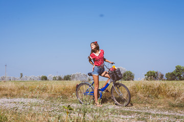Young pinup woman cycling in fields under bright blue summer sky copy space image