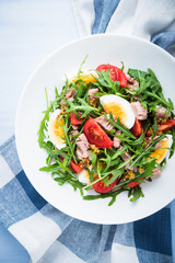 Fresh salad with tuna, tomatoes, eggs, arugula and mustard on blue wooden background top view. Healthy food.