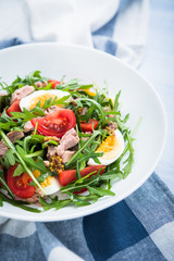 Fresh salad with tuna, tomatoes, eggs, arugula and mustard on blue wooden background close up. Healthy food.