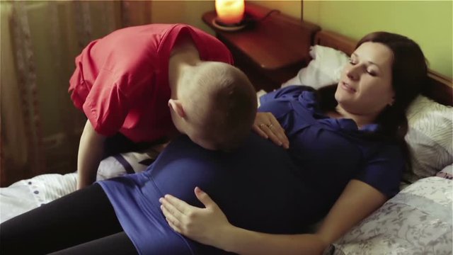 Little boy puts his ear to the big belly of a pregnant mother.