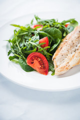 Fototapeta na wymiar Roasted chicken breast and fresh salad with tomato and greens (spinach, arugula) close up on white textured background. Healthy food.