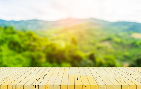 wood table and blur image of green mountain.