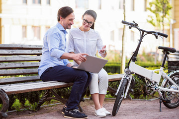 Smiling man and woman talking in park with a laptop