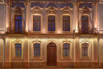 Several windows, two balconies in a row and door on night illuminated facade of urban apartment building front view, St. Petersburg, Russia.