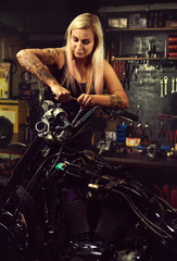Obraz na płótnie Canvas Blond woman mechanic repairing a motorcycle in a workshop