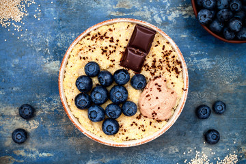 Gluten free amaranth and quinoa porridge breakfast bowl with blueberries and chocolate over vintage blue background. Top view, overhead, flat lay. Copy space