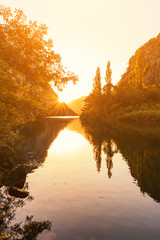 Golden sunset over the canyon of river Cetina with yellow trees, sun and reflection in a water,...