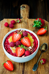 Healthy breakfast. Mango maca smoothie bowl topped with hazelnuts, oat granola, fresh berries and raspberry puree. Rustic style, vintage silverware.
