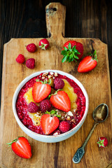 Healthy breakfast. Mango maca smoothie bowl topped with hazelnuts, oat granola, fresh berries and raspberry puree. Rustic style, vintage silverware.