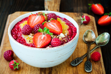 Healthy breakfast. Mango maca smoothie bowl topped with hazelnuts, oat granola, fresh berries and raspberry puree. Rustic stye, vintage silverware.