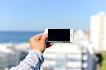 Closeup on mobile phone in the hand with blue sky on the background