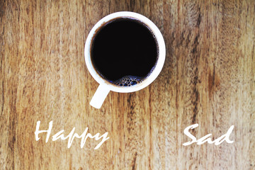 Inscription happy and sad in a cup of coffee and wooden backgrou