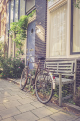 Fototapeta na wymiar Geparktes Fahrrad in Amsterdam, Parkbank und Häuserzeile, retro 
