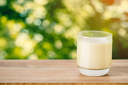 glass of milk on wooden table mock up over blurred garden bokeh in morning sun light background.
