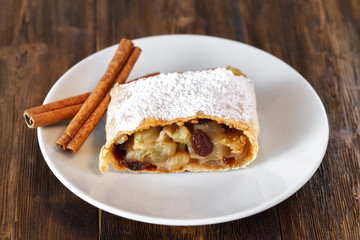 Apple strudel with icing sugar, cinnamon sticks, wooden background