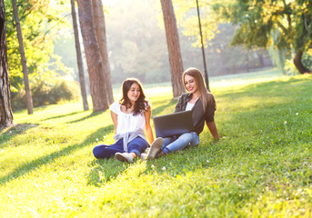 Portrait of two female student sitting in park with laptop, education and learning concept.