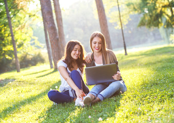 Portrait of two female student sitting in park with laptop, education and learning concept.