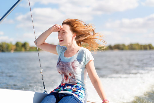 Smiling young woman sitting on sailboat, enjoying mild sunlight, sea or river cruise, summer vacation and travel concept.