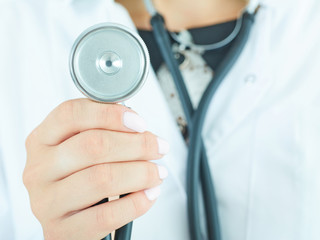 Female medicine doctor hand holding stethoscope head closeup in front of her chest. Treatment and patient care concept.