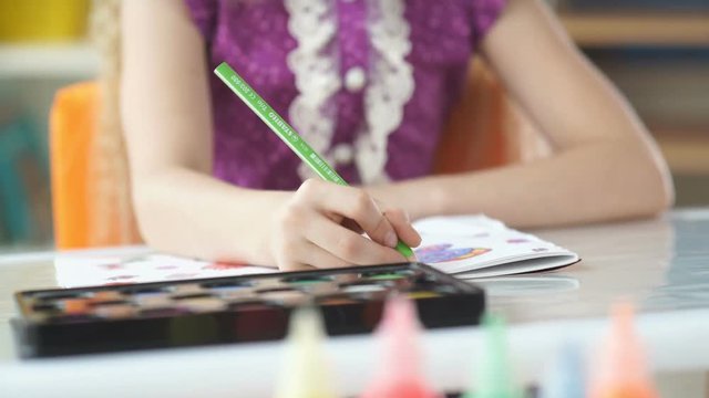 Close-up of a green pencil in a child's hand. Girl draws with crayons. The child draws. Children's entertainment.