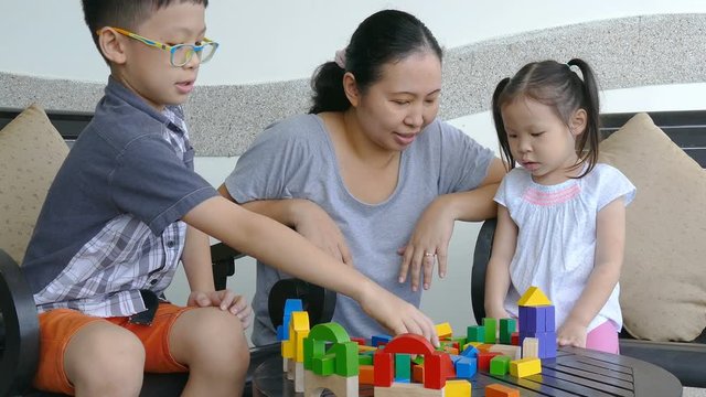 Little asian children and mother playing with colorful construction blocks on table 