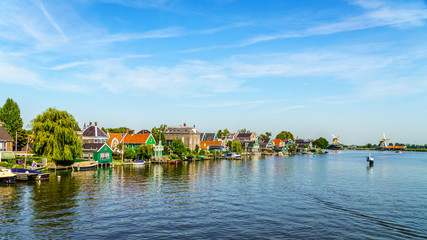 View from the Zaan River of old Dutch Windmills and historic houses along the river at the historic villages of Zaanse Schans and Zaandijk in the Netherlands