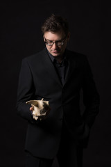 Man wearing a black suit holding an animal skull and thinking about life on earth