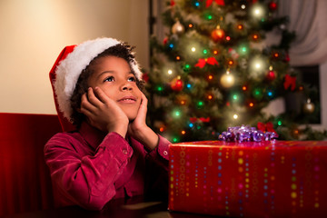 Afroamerican boy near Christmas present. Black kid beside Christmas present. Wait until it's time....