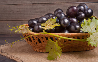 Blue grapes in a wicker basket on wooden table