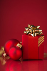 Red gift box with golden ribbons and xmas baubles on red background. Merry christmas. Space for text.