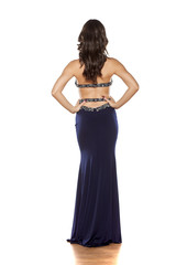 Naklejka premium back view of a young woman posing in a long blue dress on a white background