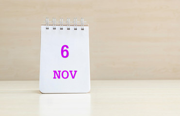 Closeup surface note book with purple 6 nov word  in page on blurred brown wood desk and wood wall textured background with copy space under window light