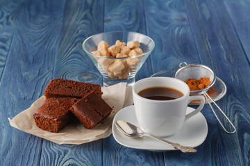 Chocolate brownie on a white plate. A coffee cup and a fork on b
