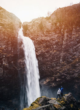 Couple in love looking at Manafossen waterfall, holding hands. Dreamy picturesque scene.