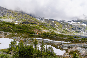 Tourist tent camping in high mountains among alpine meadow and snow.