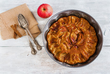Homemade apple and cinnamon cake. Pie in baking dish, vintage fork and spoon and fresh fruit on wooden background. Top view.
