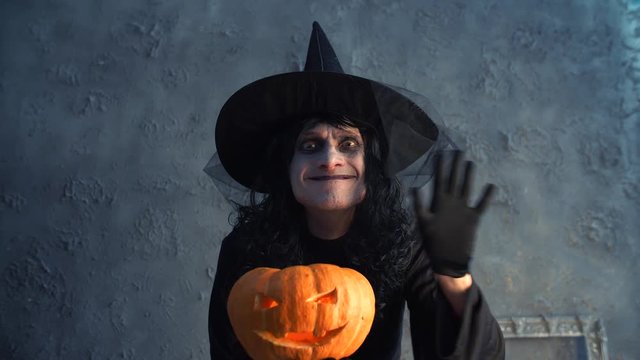 Halloween witch holding a pumpkin and waving his hand
