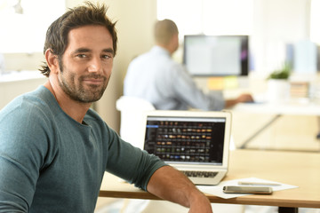 Fototapeta na wymiar Portrait of cheerful man in office working on laptop