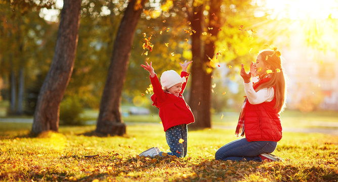happy family mother and child girl playing and throw leaves in a
