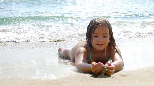 Little girl lying on the sand, the sea waves splashing in her body