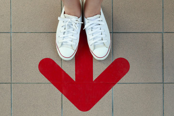 Woman legs wearing white shoes standing behind the red arrow line